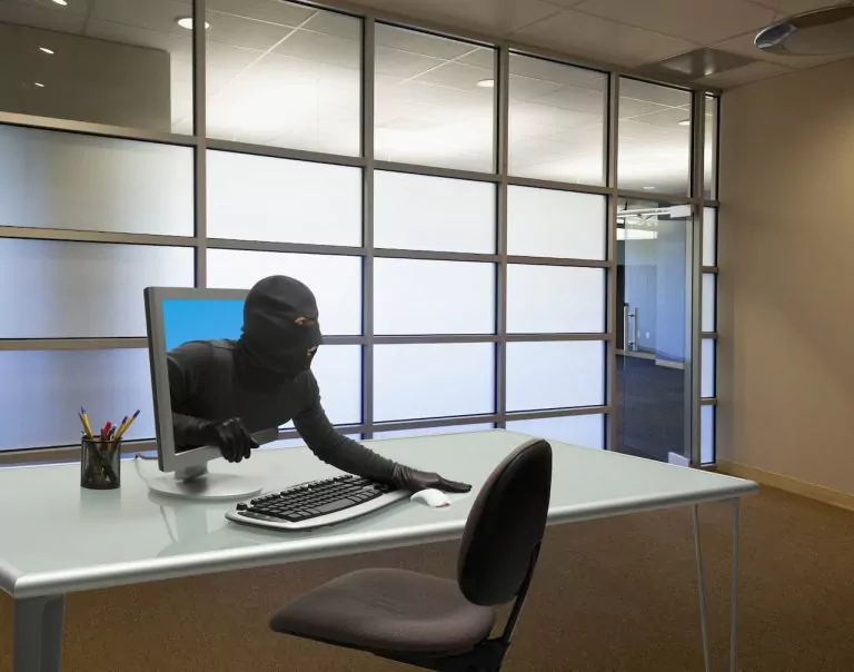 A suspicious figure emerging from a computer screen in an office