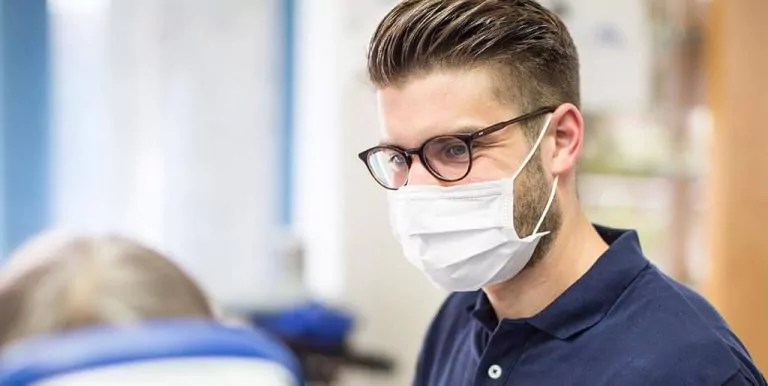 Dentist in navy shirt with a mask, focused on patient in a clinical setting.
