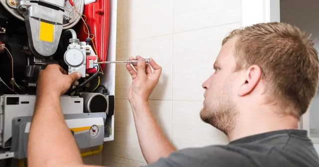 Engineer adjusting boiler component with a wrench in a tiled room, focused on task with visible internal mechanisms.
