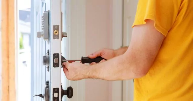 Person using a screwdriver to adjust a lock on a white door with multiple locks and keypad.