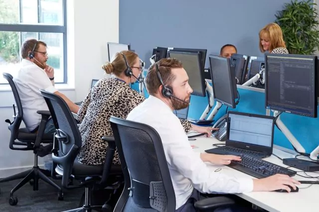 Team of professionals wearing headsets, seated at desks and looking at their monitors in a modern office.