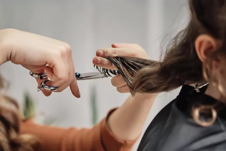 Hairdresser cutting long hair with scissors in a salon, focusing on the hands and hair, with a blurred background.