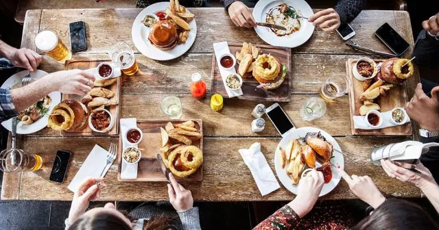 Overhead view of a table with people enjoying lunch or dinner, surrounded by various dishes and drinks.