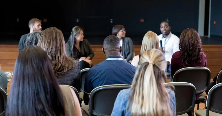 Audience at a sports community centre, facing a panel of four individuals.