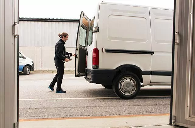 Delivery driver behind a white commercial parked van with an open back door.