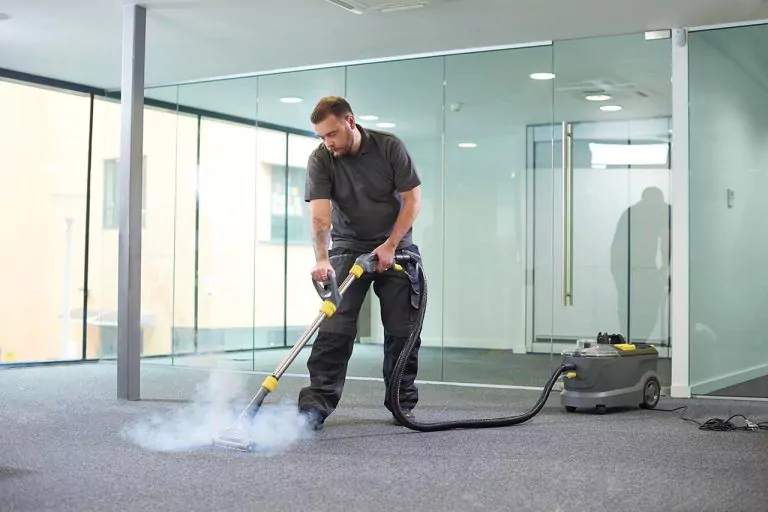 Man cleaning a grey carpet with a steam cleaner in a modern office, steam rising.