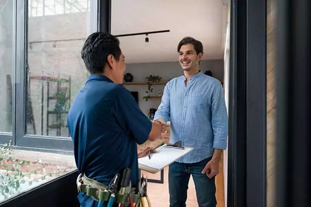 Contractor shaking hands with a customer outside a house, both smiling in a friendly, professional exchange.