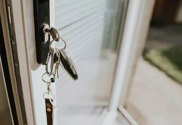 Keys inserted into a door lock, with green grass visible outside.