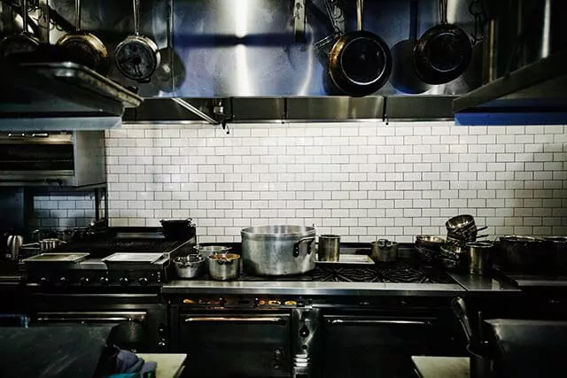 Professional kitchen with stainless steel equipment, including ovens, counters, and ventilation hoods.