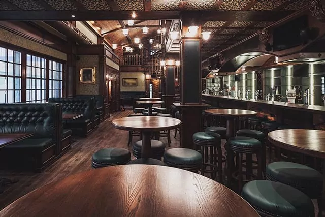 Interior of a bar showcasing rustic wooden tables and stools, with a warm and inviting atmosphere.