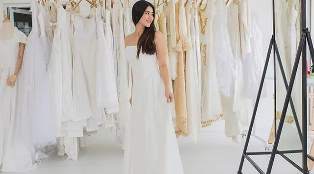 Woman in a white wedding dress standing before racks of dresses in a wedding dress store.
