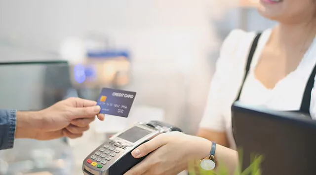 Person handing a credit card to a cashier in a shop's checkout counter.