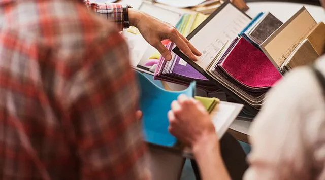 Two people examining fabric swatches and documents at a furniture shop, with colorful fabric on the table.