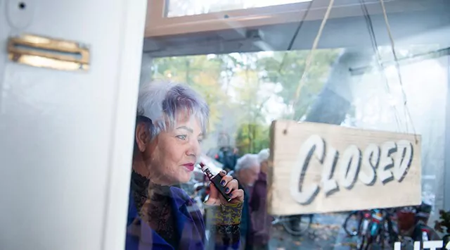 Woman holding a vape inside a store with a "Closed" sign on the door.