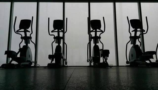 Four elliptical machines lined up in a dimly lit gym. Only the shape of the equipment is visible.