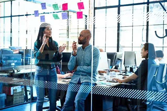 Two IT consultants in a modern office having a meeting with sticky notes on the glass wall in front of them.