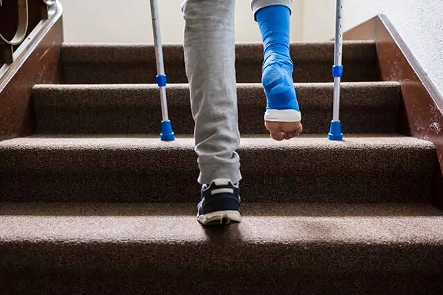 Person with blue cast on crutches ascending a staircase, wearing sweatpants and a trainer on their left foot.