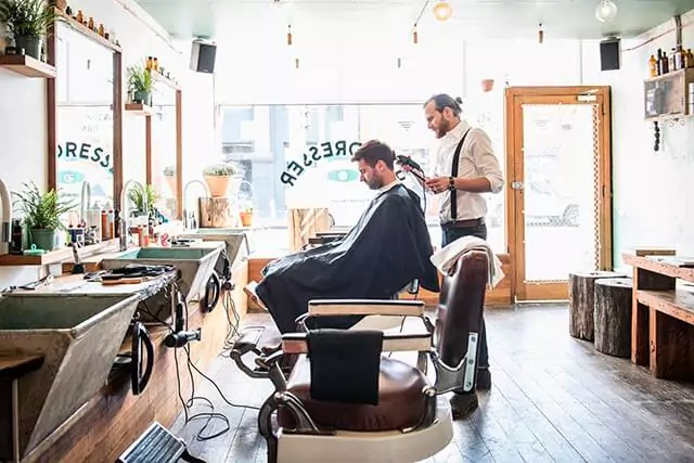 Inside a barbershop, a man sits in a chair as a barber skilfully cuts his hair.