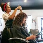 A hairstylist trims a woman's hair, showcasing a professional salon environment.